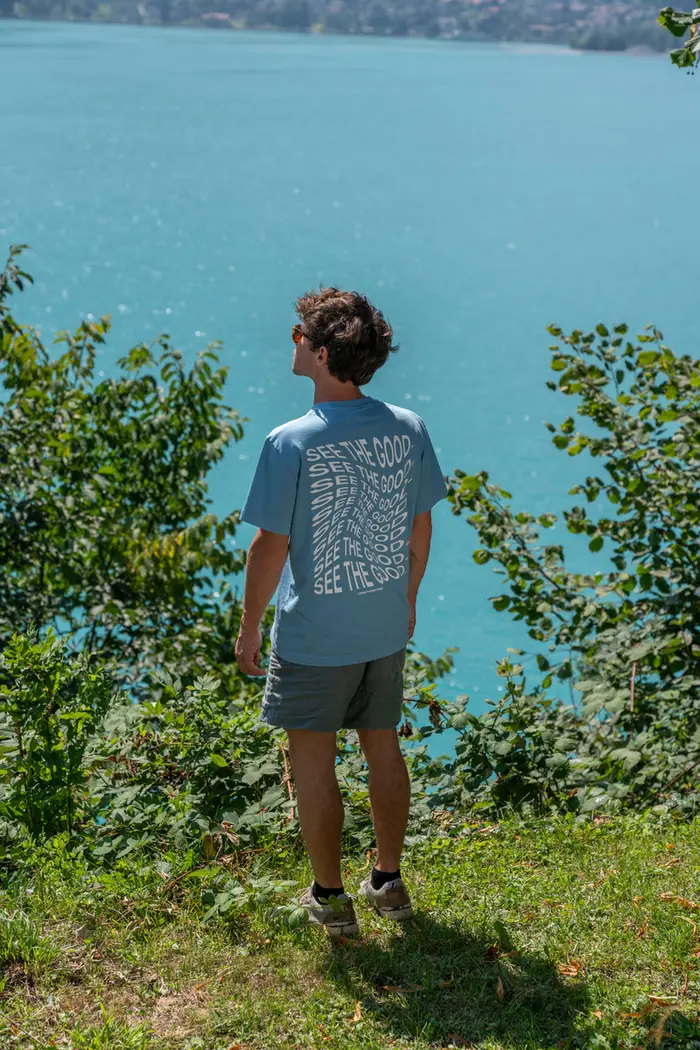 Mann im hellblauen See the Good Tee blickt über den Bergsee